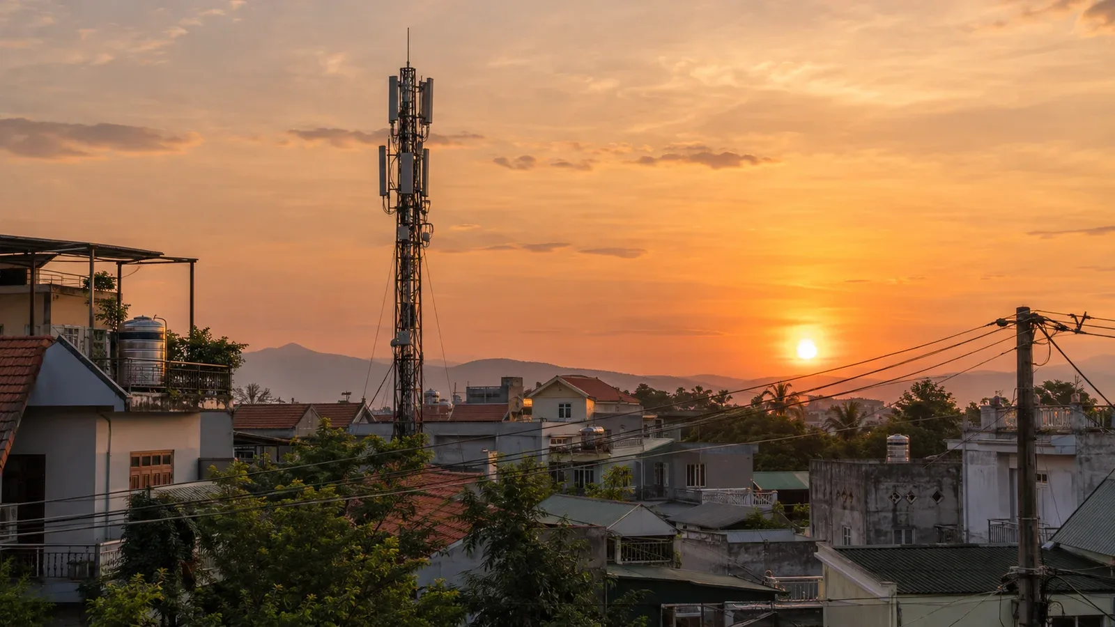 Trạm phát sóng di động với các tấm ăng-ten nhô lên trên những ngôi nhà thấp ở một thị trấn Việt Nam lúc hoàng hôn